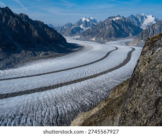 A dramatic high-angle shot of the Ruth Glacier, a massive frozen river of ice flowing through a mile-deep granite gorge. The image highlights the lateral moraines and compression zones of the glacier, with the jagged peaks of the Alaska Range towering in the background.