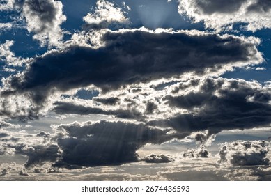 Dramatic, high-contrast cloudy sky with rays of sunlight shining through the clouds from the hidden sun behind them