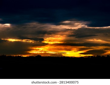 a dramatic and high-contrast sunset over a flat, silhouetted horizon line.