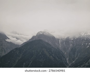 Dramatic Himalayan mountain peaks covered with mist and clouds above deep forested valley landscape.