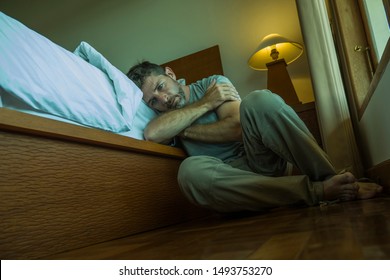 dramatic home portrait of young depressed and desperate man sitting on bedroom floor next to bed suffering depression and anxiety feeling overwhelmed and helpless