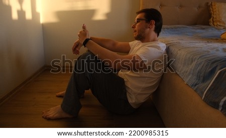 dramatic home portrait of young depressed and desperate man sitting on bedroom floor next to bed suffering depression and anxiety feeling overwhelmed and helpless with phone