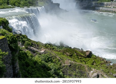 A dramatic horizontal close-up shot of the torrent of water cascading over the crest of American Falls at Niagara. Huge clouds of thick white mist rise from the bottom, contrasting with the lush green mossy rocks on the cliff edge. Perfect for themes of raw power, natural energy, and environmental wonder.