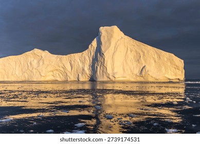 Dramatic Iceberg with Golden Reflection During Midnight Sun in Greenland Arctic Waters