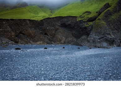 Dramatic Icelandic landscape featuring moss-covered basalt cliffs, columnar rock formations, and black volcanic sand beach with lush green