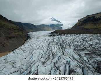 Dramatic Icelandic landscape of glacier tongue spurting off ice cap, with a glacial wall in the background on the gloomy winter day, drone shot.