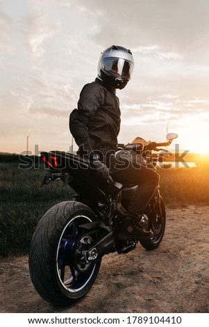 Dramatic image of biker sitting on motorcycle in sunset on the country road.