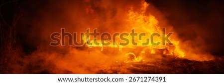 A dramatic image of a car engulfed in flames at night. Vivid oranges dominate, highlighting the destruction. Ideal for concepts of danger, emergency, or drama. Wide banner.