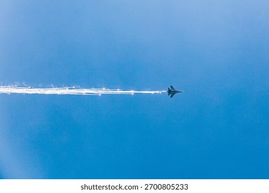 Dramatic image of a fighter jet deploying brilliant flares while climbing rapidly into a vast blue sky. High-impact action and vivid contrast.