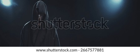 Dramatic image of a hooded figure in shadowy lighting, dark tones, perfect for mysterious themes. Wide banner format with copy space ideal for text placement.