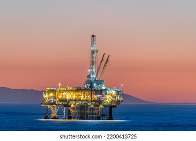 Dramatic image of an offshore oil platform off the coast of California against a pink winter sky as the sun sets and the rig's lights illuminate.  - Shutterstock ID 2200413725