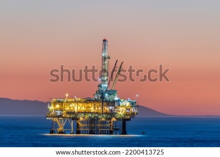 Dramatic image of an offshore oil platform off the coast of California against a pink winter sky as the sun sets and the rig's lights illuminate. 



