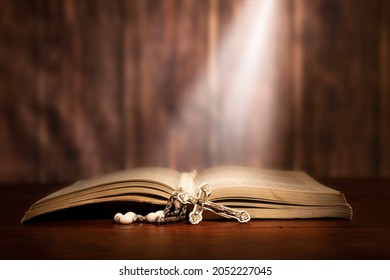 Dramatic image showing a bright light beam shining on an old bible with a rosary laying in front of it. - Shutterstock ID 2052227045