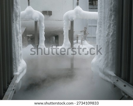 A dramatic image showing foam being expelled from a fire suppression system, with thick white foam enveloping pipes and creating a misty, fog-like atmosphere. The foam is used in industrial settings for fire protection, and the image captures both the force and efficiency of the system in action. This is an ideal visual for topics related to fire safety, emergency systems, and industrial technologies.