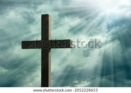 Dramatic image showing a religious church cross framed against a moody sky that is beginning to open and pierce light through behind the cross, showing the Lord's presence. 

