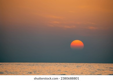 A dramatic image of the sun setting in a blaze of glory. The sun is a fiery orb, surrounded by a halo of orange and red light. The sky is ablaze with color, from the deep blue of the ocean to red ...