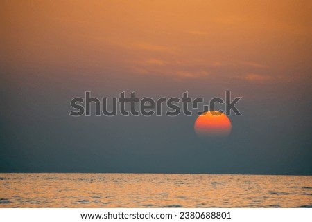A dramatic image of the sun setting in a blaze of glory. The sun is a fiery orb, surrounded by a halo of orange and red light. The sky is ablaze with color, from the deep blue of the ocean to red ...