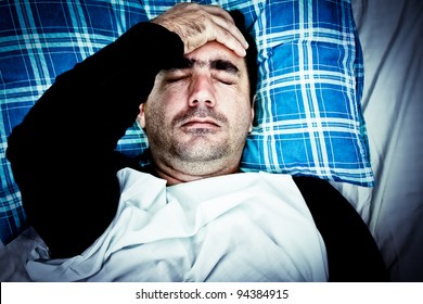 Dramatic image of a very stressed or mentally disturbed man suffering a headache laying in bed