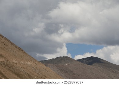 A dramatic and intense scene where deep, brooding clouds engulf towering mountain peaks, creating an atmosphere. The dark clouds swirl ominously, casting eerie shadows on the rugged landscape below.