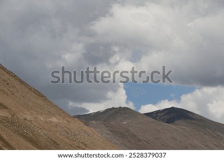 A dramatic and intense scene where deep, brooding clouds engulf towering mountain peaks, creating an atmosphere. The dark clouds swirl ominously, casting eerie shadows on the rugged landscape below.