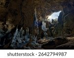 Dramatic interior of a natural cave in Spain, featuring striking stalagmites and stalactites illuminated by natural light pouring in through a large opening in the cave ceiling. Underground landscape.
