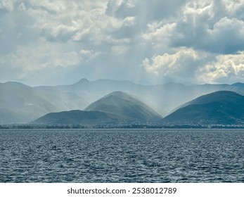 Dramatic lakeside scene at Lake Ohrid, North Macedonia. Stormy sky casting shadows over hills and mountains. Brewing storm with dark clouds accumulating. Power and beauty of nature. Boat tour - Powered by Shutterstock