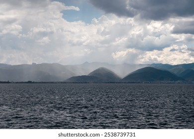 Dramatic lakeside scene at Lake Ohrid, North Macedonia. Stormy sky casting shadows over hills and mountains. Brewing storm with dark clouds accumulating. Power and beauty of nature. Boat tour - Powered by Shutterstock