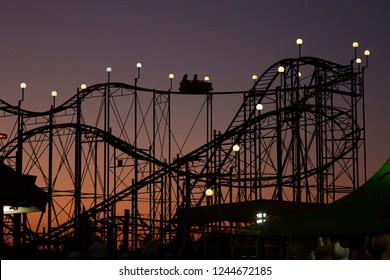 Dramatic landscape of county fair rollercoaster ride silhouette at sunset 