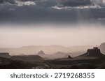 A dramatic landscape with dark clouds looming over distant mountains and a river running through ita