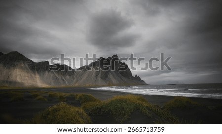 Dramatic landscape of dark mountains and cloudy sky. Rugged mountains meet the ocean. Stormy clouds hover over the mountains, creating a moody atmosphere. Iceland nature and travel image.