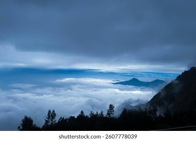 A dramatic landscape featuring a dense layer of clouds obscuring the valley below, with mountain peaks rising above.