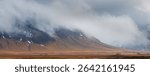 Dramatic landscape featuring low clouds obscuring majestic mountains in iceland, with small houses nestled in the foreground. Icelandic landscape