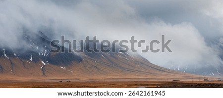 Dramatic landscape featuring low clouds obscuring majestic mountains in iceland, with small houses nestled in the foreground. Icelandic landscape