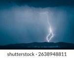 A dramatic landscape featuring a powerful lightning strike illuminating a dark sky over distant hills with city lights below.