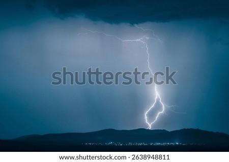 A dramatic landscape featuring a powerful lightning strike illuminating a dark sky over distant hills with city lights below.