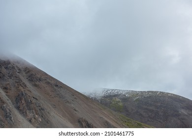 Dramatic landscape with high mountain range in rainy low clouds. Bleak alpine scenery with mountain range in low gray cloudy sky. Gloomy mountain view to large rocky hills with snow among gray clouds. - Shutterstock ID 2101461775