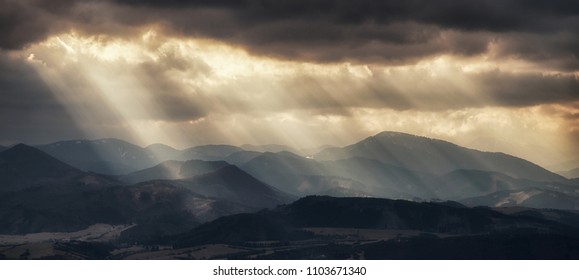Dramatic landscape of mountains with sunlight beams breaking through dark clouds, scenic view of sun rays and nature background