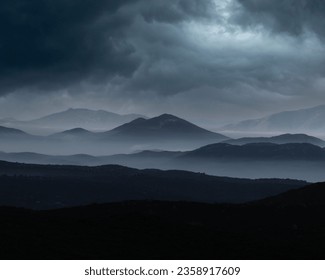 Dramatic landscape of rocky mountains shrouded in dark, cloudy skies with a gray overcast - Powered by Shutterstock