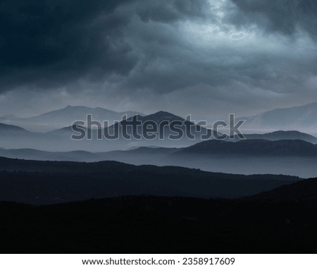 Dramatic landscape of rocky mountains shrouded in dark, cloudy skies with a gray overcast
