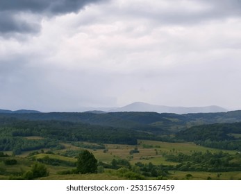 A dramatic landscape with rolling hills covered in lush green forests. The sky is filled with dark, stormy clouds, creating a sense of tension and anticipation. - Powered by Shutterstock