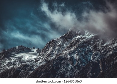 Dramatic landscape of rugged mountains covered with snow, viewed from low angle with dark clouds in foreground. Wild nature of New Zealand