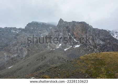 Dramatic landscape with sharp pinnacle on high mountain range in rainy low clouds. Bleak alpine scenery with peaked mountain top in low gray cloudy sky. Gloomy view to large pointy top in gray clouds.