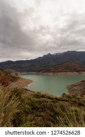 Dramatic landscape with the sky covered by dark clouds and turquoise lake surrounded by mountains covered with pine forests. Copy space.
