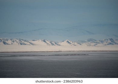 Dramatic landscape with snow mountain under blue cloudy sky. Pastel colors, snow-capped mountains over a mountain lake, they look like a mirage. Winter landscapes of Mongolia. 