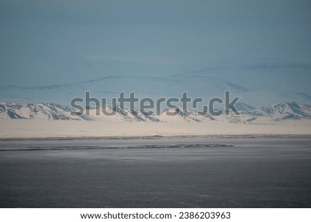 Dramatic landscape with snow mountain under blue cloudy sky. Pastel colors, snow-capped mountains over a mountain lake, they look like a mirage. Winter landscapes of Mongolia. 
