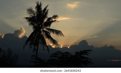 Dramatic landscape with sun rays piercing through thick dark clouds over a tropical forest and distant mountains. Ideal for themes of hope, peace, nature, and spirituality.