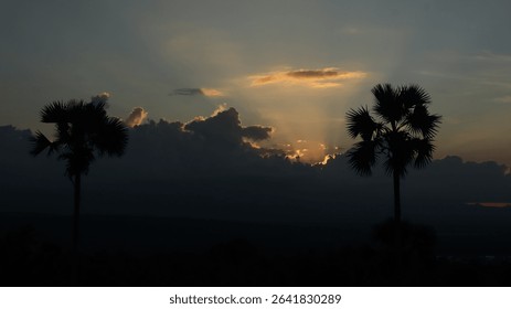 Dramatic landscape with sun rays piercing through thick dark clouds over a tropical forest and distant mountains. Ideal for themes of hope, peace, nature, and spirituality.