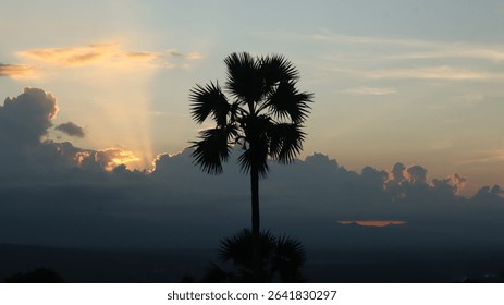 Dramatic landscape with sun rays piercing through thick dark clouds over a tropical forest and distant mountains. Ideal for themes of hope, peace, nature, and spirituality.