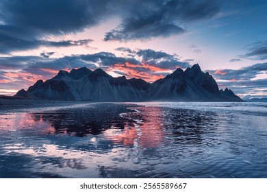 Dramatic landscape of sunset sky over volcanic Vestrahorn mountain reflecting on black sand beach in summer at Stokksnes peninsula, Iceland