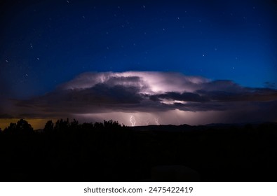 Dramatic late evening cumulus cloud brilliantly lit up by a lighting storm with star trails in the blue sky above